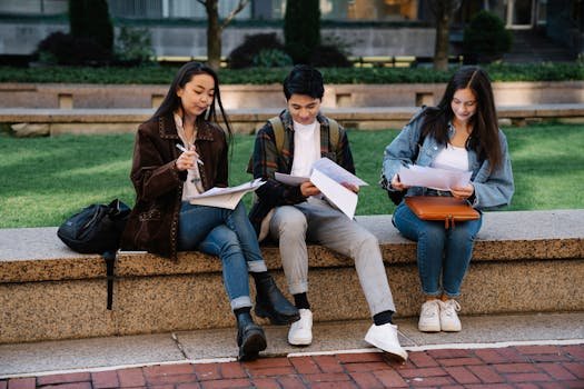 Three students studying together on a bench in a university campus setting outdoors.
